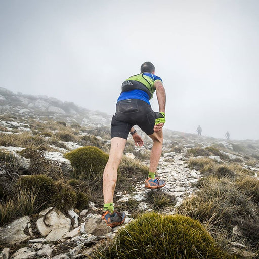 גבר עולה על הר לבוש גרביים לריצות שטח ארוכות לורבל TRACK בצבע ירוק זוהר| יוניסקס